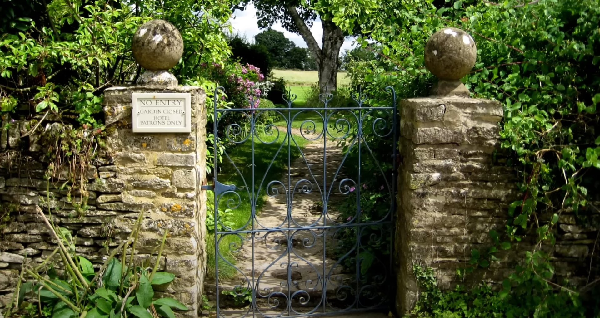 Classic landscape design featuring natural stone construction and established garden beds Traditional garden entrance with stone pillars, ornate metal gate, and mature plantings
