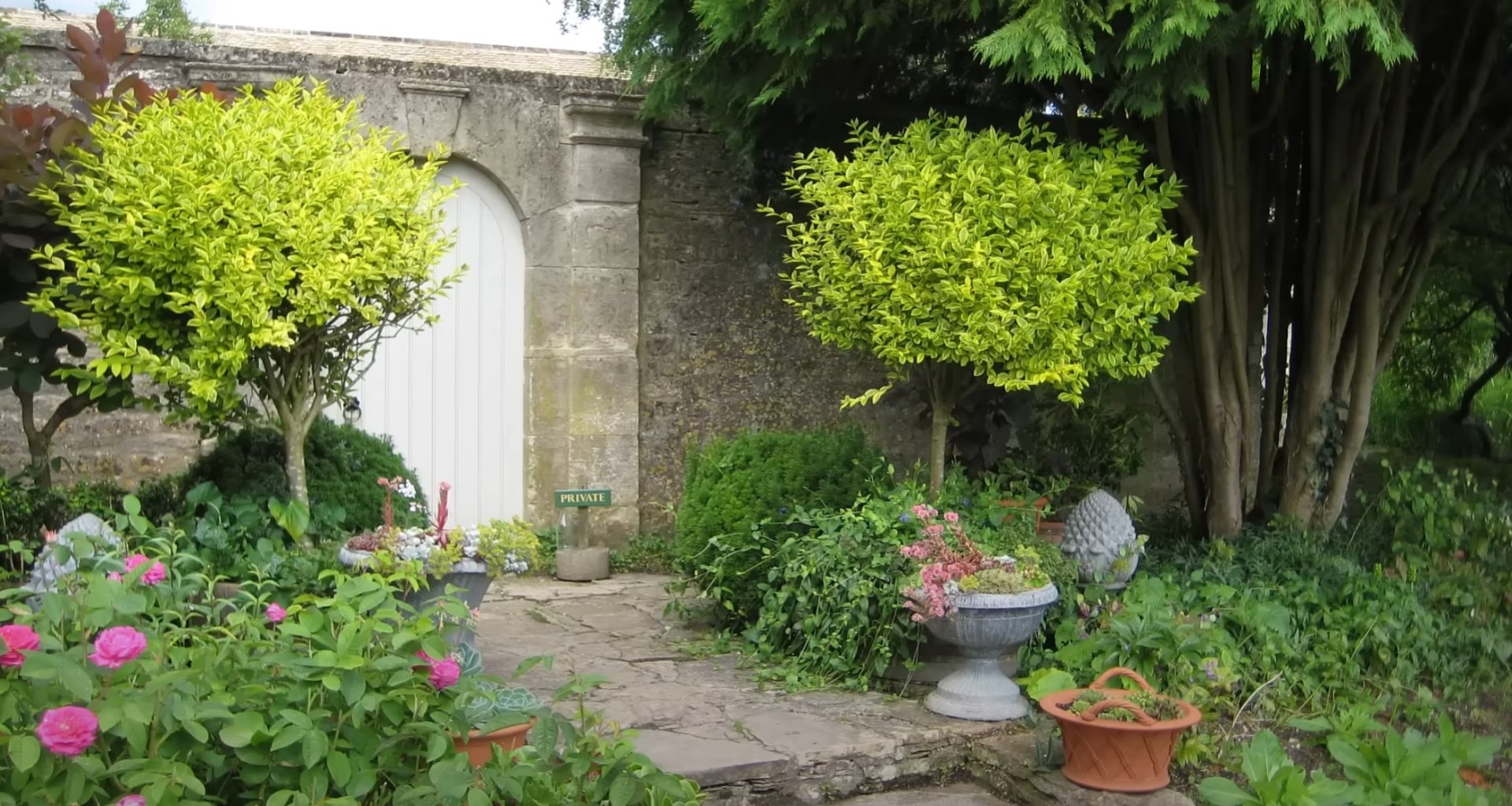 Traditional garden design with formal entrance and colorful seasonal plantings Charming garden entrance with stone archway, lush plantings, and decorative containers