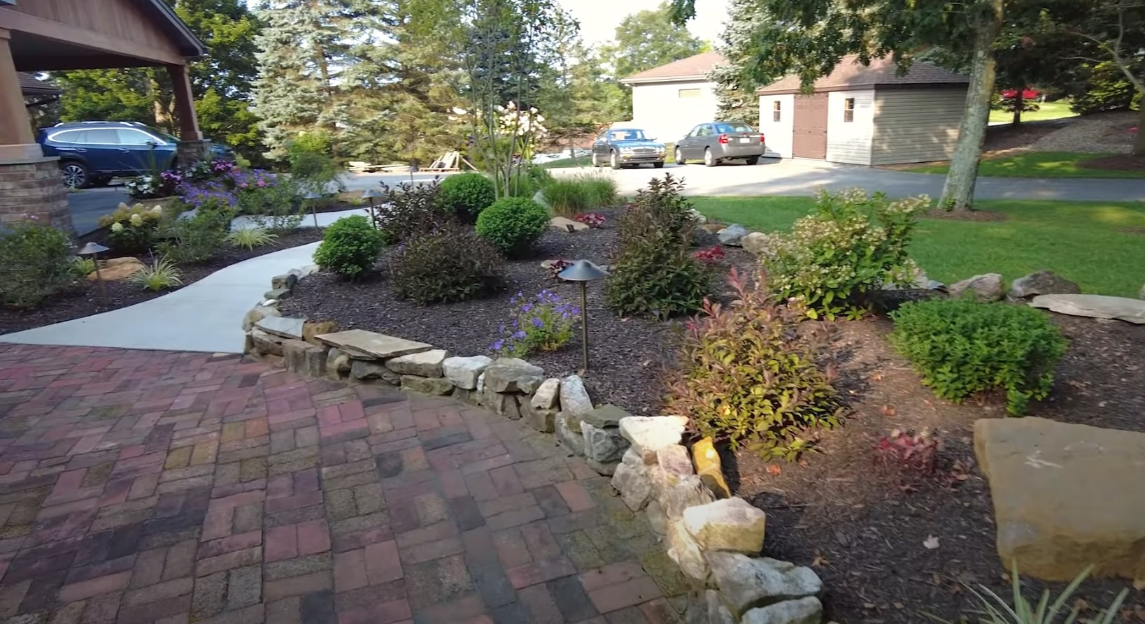 Custom landscape design featuring natural stone hardscaping and colorful seasonal plantings Beautiful front yard landscaping with stone retaining walls, diverse plantings, and paver walkway