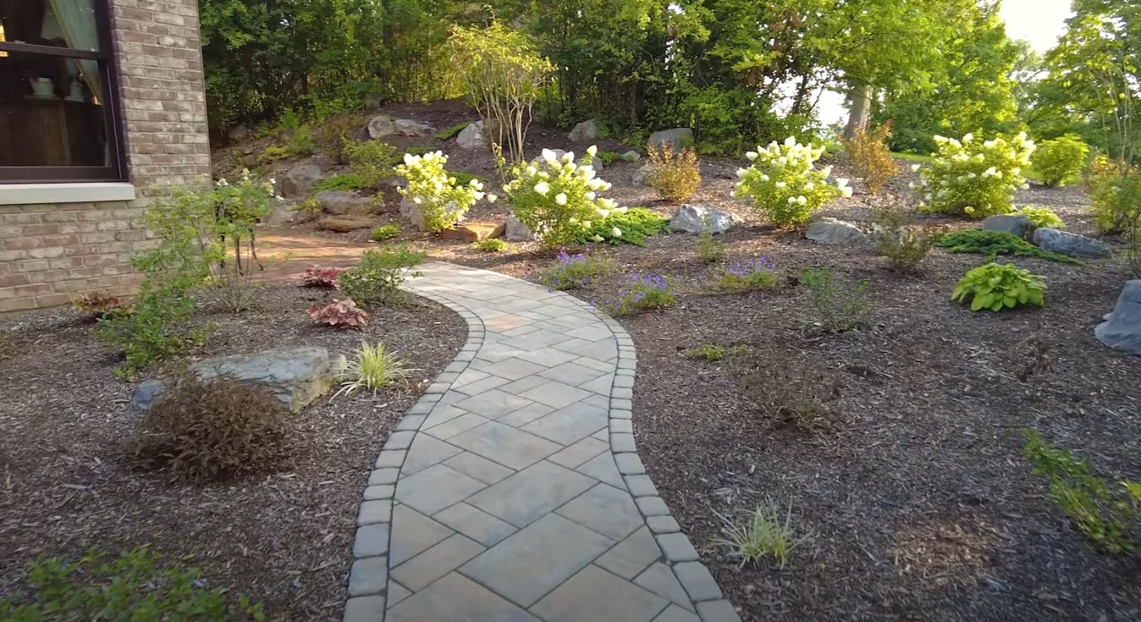 Custom hardscaping and landscape design featuring natural stone walkways Elegant stone pathway through professionally landscaped garden with hydrangeas and ornamental plants